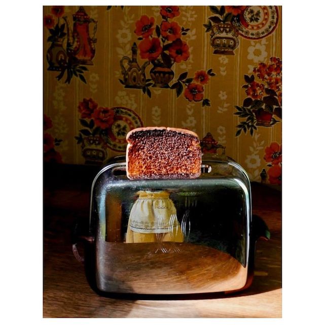 Burn toast popping out of a stainless steel toaster, with a reflection of an apron belonging presumabely to the photographer.