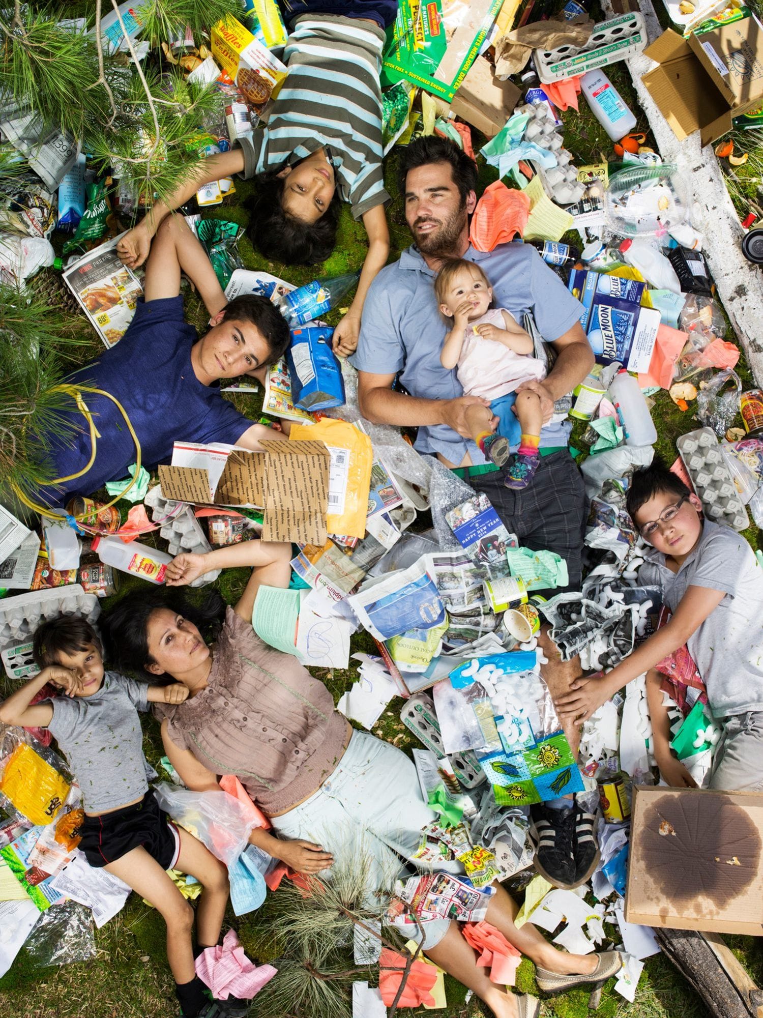 A family lying on the grass surrounded by a week's worth of trash.