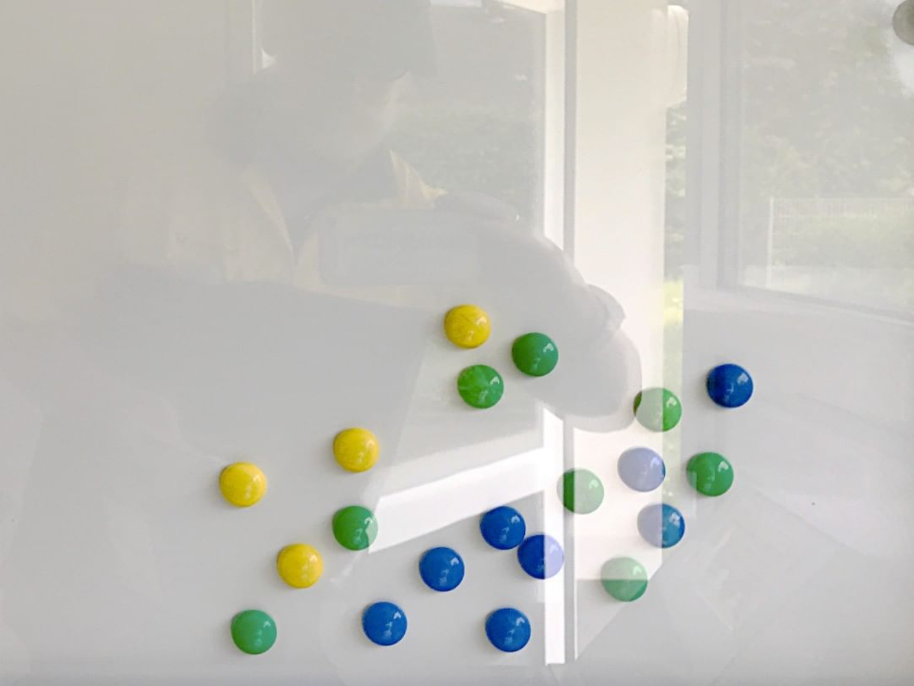 a person's reflection on a whiteboard with coloured magnets